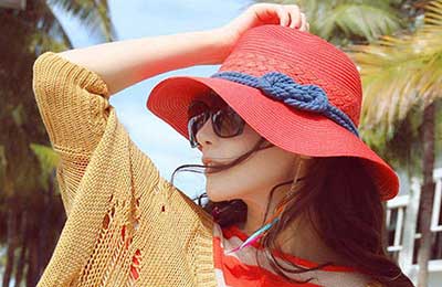 دختر زیبا با کلاه قرمز با نواری آبی و عینک آفتابی در حالی که دست خود را روی کلاهش گذاشته به دوردست خیره شده