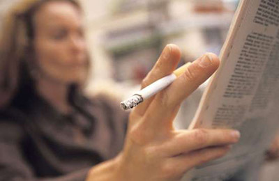 زن میانسال در حالی که یک سیگار بین انگشتان خود دارد در حال روزنامه خواندن
