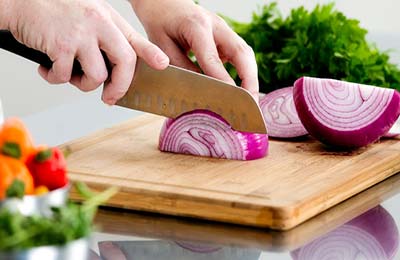 دستانی در حال خرد کردن پیاز با یک چاقوی پهن روی یک تخته آشپزی 