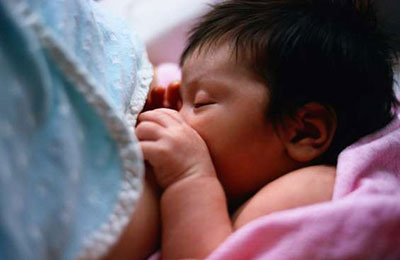 نوزادی با موهای سیاه و پرپشت در حال شیر خوردن از سینه