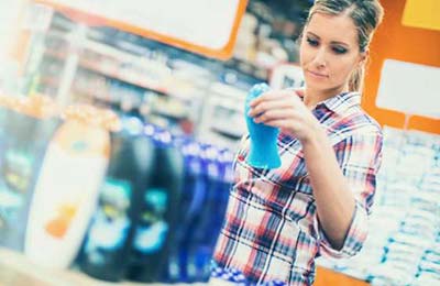 زن با لباس چهارخانه در فروشگاه با یک قوطی آبی رنگ شامپو در دست