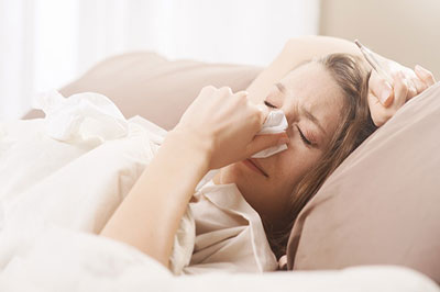 یک زن بیماربا موهای روشن در حالی که بر روی تخت خوابیده و دستمالی در دست دارد