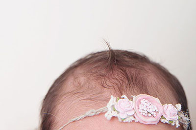 سر یک نوزاد با یک تل بر روی آن که با شکوفه‌های صورتی و سفید تزیین شده است