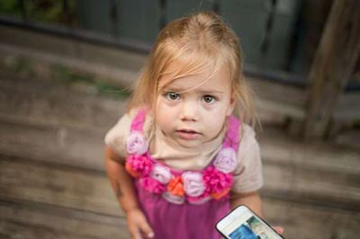 دختر خردسال زیبا با یک موبایل در دستش به بالا نگاه می‌کند