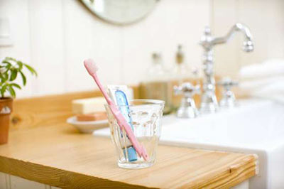 یک مسواک صورتی و یک خمیردندان آبی داخل یک لیوان شیشه‌ای در کنار سینک دستشویی