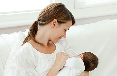 یک زن با موهای بلند و مشکی که از پشت سر بسته شده در حال شیر دادن به نوزادش