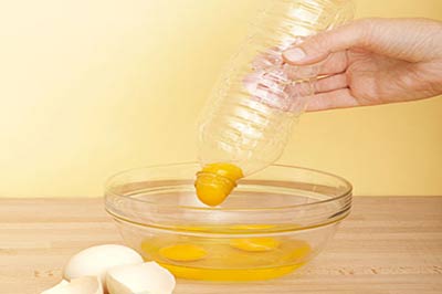 یک دست در حالیکه بایک قوطی پلاستیکی یک زرده تخم مرغ را از داخل یک کاسه پیرکس بیرون می آورد 