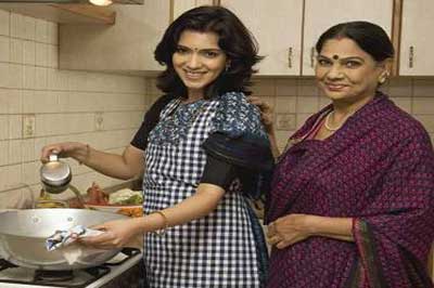 زن جوان هندی با لباس سنتی هند در حال آشپزی در آشپزخانه در کنار زن مسن هندی با ساری بنفش