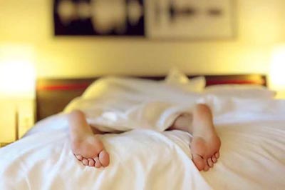 پاهای یک زن در حالی که به شکم روی تخت با ملحفه های سفید دراز کشیده است