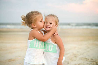دو دختر خردسال در حالی که یکی دیگری را در آغوش گرفته و گونه‌اش را می‌بوسد و دیگری لبخند می‌زند
