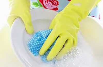 دستهای یک زن با دستکش که با اسفنجی آبی رنگ، بشقاب سفید رنگ را می‌شوید