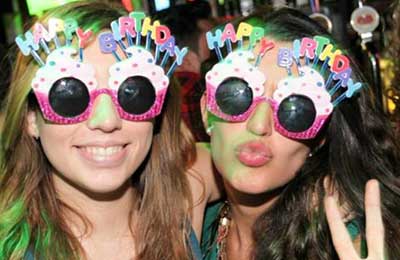 تصویر دو دختر جوان که عینکهای رنگی با نوشته تولدت مبارک به چشم دارند . یکی لبخند می‌زند و دیگری لبهای خود را غنچه کرده است
