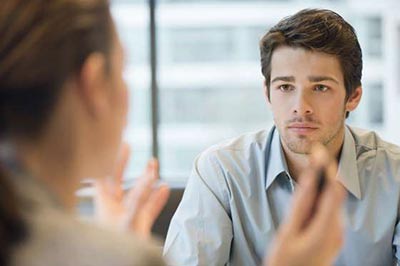 مردی جوان با موهای قهوهای و ته ریش با پیراهنی آبی در حال حرف زدن با یک زن