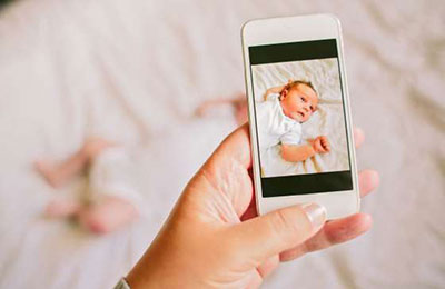 دست یک زن در حال عکس انداختن با گوشی موبایل از نوزادی که روی تخت خوابیده است