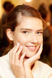دختری جوان با پوستی روشن و موهای قهوهای روشن که با فرق یک طرفه از پشت بسته شده و دستان دختر زیر چانهاش قرار گرفته