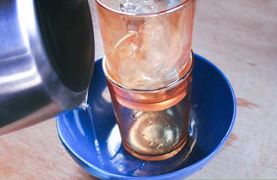 دو لیوان داخل هم که درون یک کاسه آبی رنگ گذاشته شده‌اند و داخل یکی از آنها یخ ریخته شده است