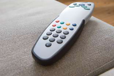 یک کنترل تلویزیون نقره‌ای و مشکی روی یک مبل طوسی