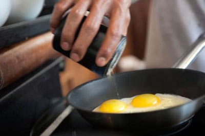 دستی در حال پاشیدن نمک روی دو عدد تخم مرغ درون یک ماهیتابه سیاه