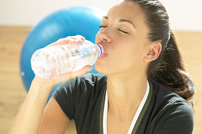 زن با لباس ورزشی در حال نوشیدن آب از بطری