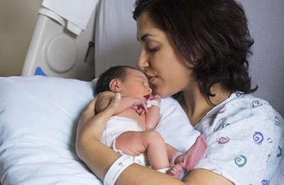 زنی بر روی تخت بیمارستان ، نوزادش را روی یک بالش در آغوش گرفته و می‌بوسد