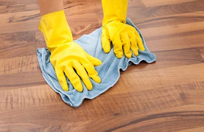 دستانی با دستکش‌های زرد در حال پاک کردن پارکت با یک دستمال آبی
