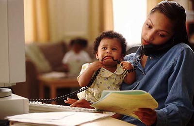 زن سیاه پوست در حال حرف زدن با تلفن در حالی که پوشه‌ای در دست  و دختر کوچکش را در آغوش دارد و بچه در حال خوردن سیم تلفن است