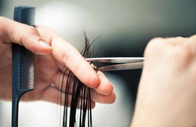 زنی در حال کوتاه کردن مو با استفاده از یک قیچی استیل و یک شانه ریز مشکی