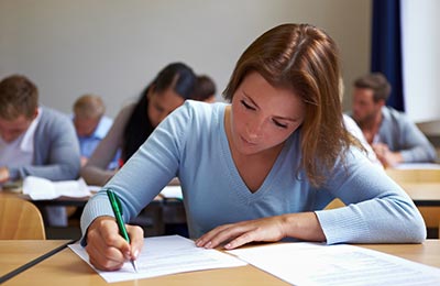 زن با لباس آبی رنگ و موهای لخت بلند در حالی که در کلاس نشسته و مشغول یادداشت برداری است