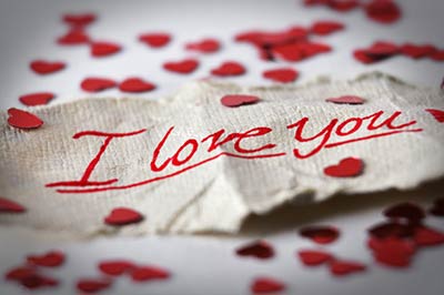یک یادداشت عاشقانه با نوشته دوستت دارم بر روی یک تکه پارچه کرم رنگ که در اطراف آن قلبهای کاغذی کوچک پراکنده شده